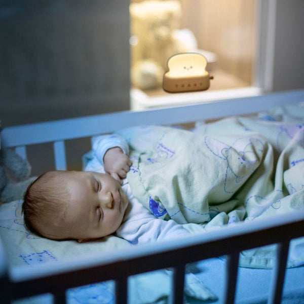 Veilleuse Grille Pain éclairant doucement un bébé endormi dans son berceau.