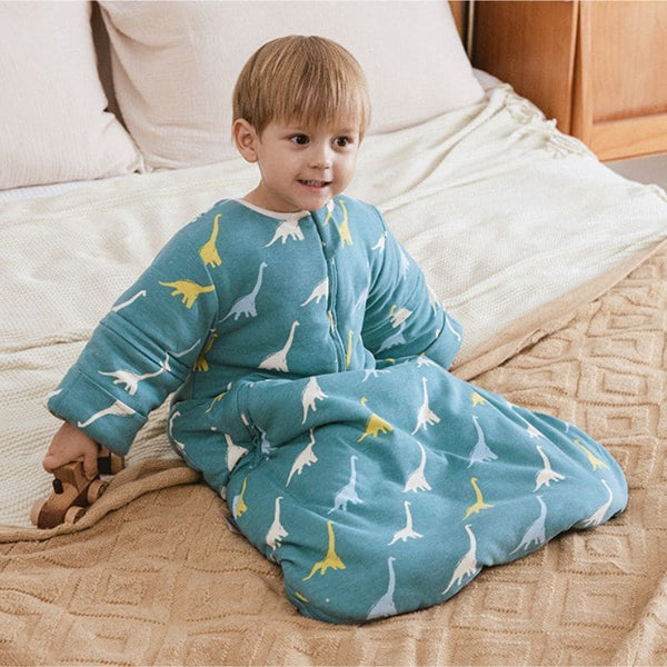 Enfant assis portant une Gigoteuse Hiver bleue à motif dinosaures colorés
