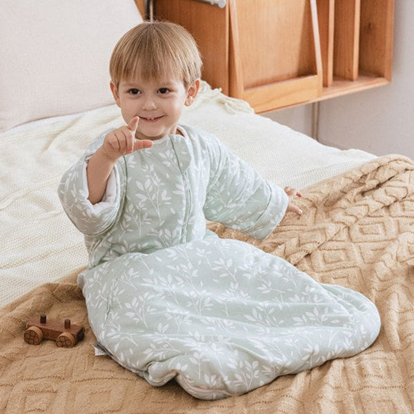 Enfant assis sur un lit portant une Gigoteuse Hiver vert sauge à motif végétal