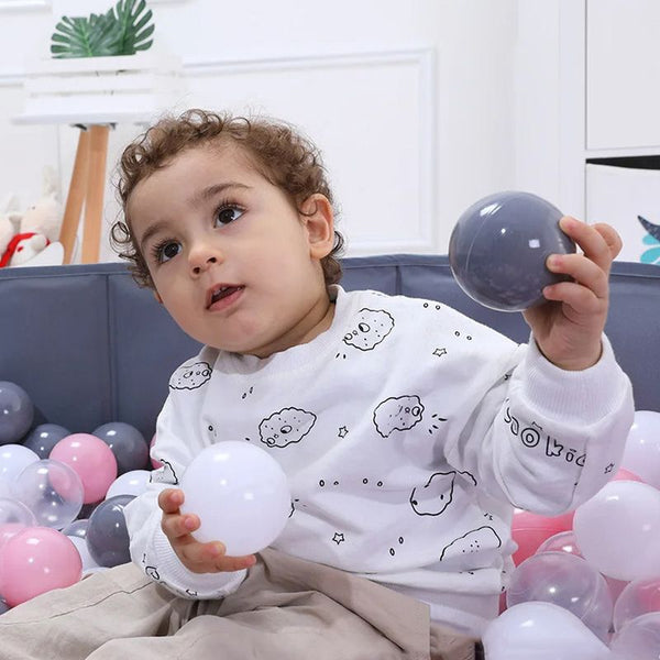 Bébé tenant une balle dans une piscine à balles bébé stimulante.