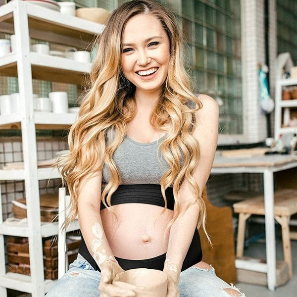 Femme souriante portant une Ceinture de Soutien de Grossesse noire dans un atelier de poterie.