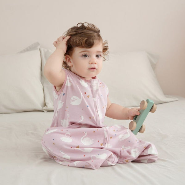 Bébé assis sur un lit en gigoteuse légère d’été motif cygnes roses