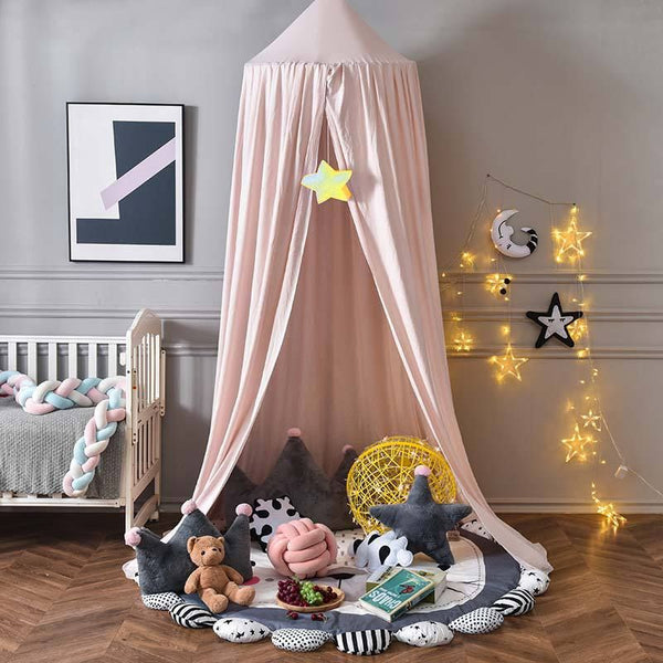 Ciel de lit bébé rose dans un espace de jeu avec des coussins et des décorations étoilées.