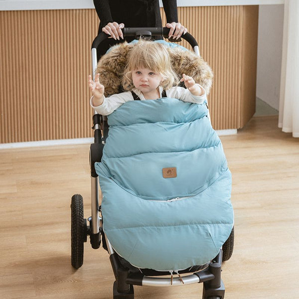 Petite fille dans une poussette équipée de la chancelière universelle évolutive FlexiCocon bleue, col en fourrure pour plus de chaleur.