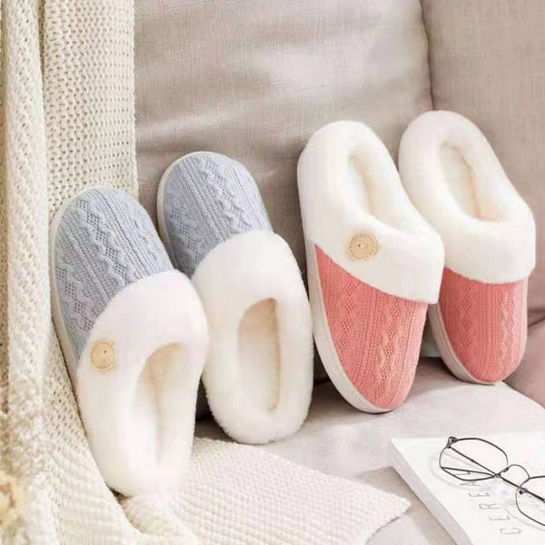 Deux paires de chaussons fourrés Femme en rose et gris posées sur un canapé dans un environnement très chic.
