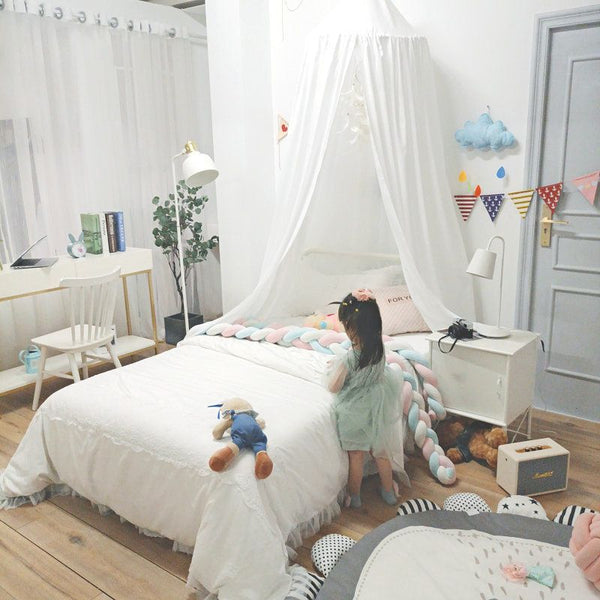 Ciel de lit bébé blanc dans une grande chambre chic avec une petite fille jouant à côté du lit.