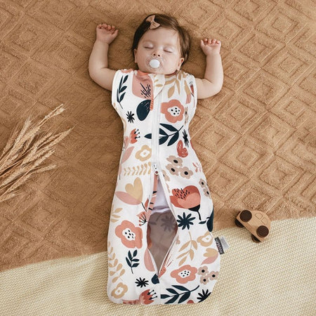 Bébé endormi portant un Lange d’Emmaillotage à fleurs pastel sur tapis beige