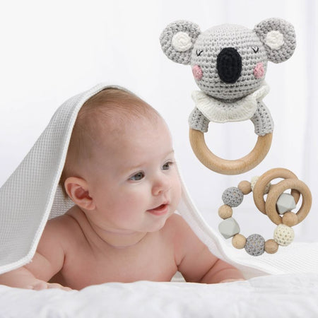 Anneaux de dentition bébé Koala et hochet en bois à côté d'un bébé allongé sur le ventre