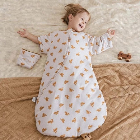 Enfant allongé et souriant dans une Gigoteuse Hiver imprimée feuilles dorées