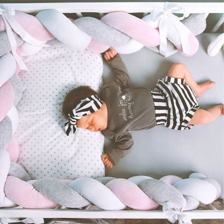 Bébé paisiblement endormi dans un lit avec une tresse de lit bébé Gris-Blanc-Rose.