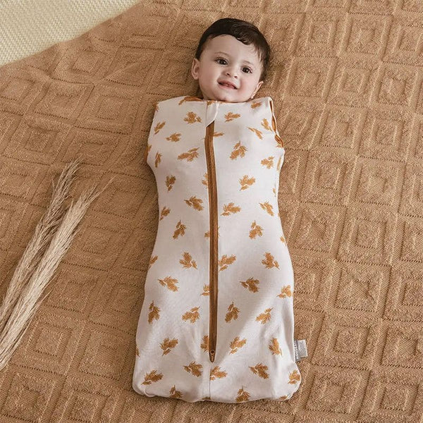 Bébé souriant emmailloté dans un Lange d'Emmaillotage EcoWrap motif nature.