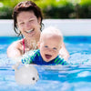 Un bébé et une adulte dans une piscine interagissant avec le Jouet de bain bébé Luna la baleine, le jouet flottant.