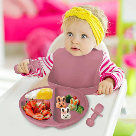 Image d’un bébé utilisant un set repas pour bébé, avec un bavoir, une assiette et des couverts en silicone.