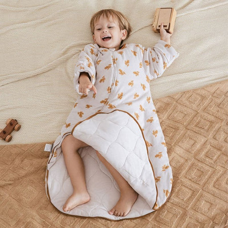 Enfant allongé avec une Gigoteuse Hiver crème motif feuilles dorées ouverte